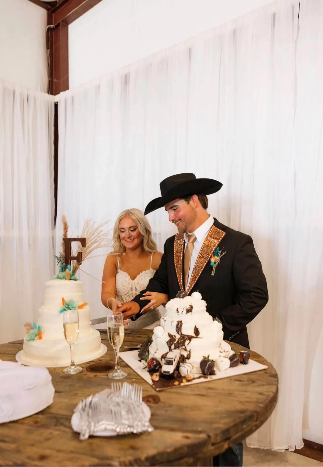 Bride and groom cutting a western-styled wedding cake in the draped barn reception hall at Reverie at Diamond D