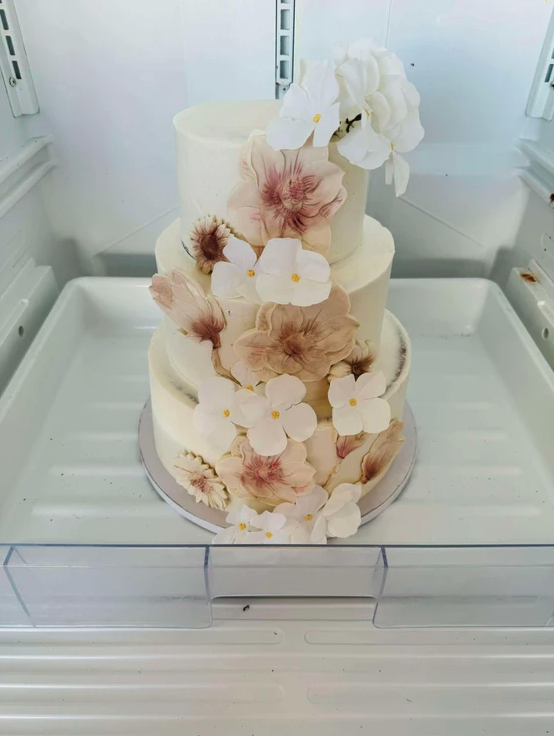 Three-tier white wedding cake with blush sugar florals for a 2024 wedding at Reverie at Diamond D