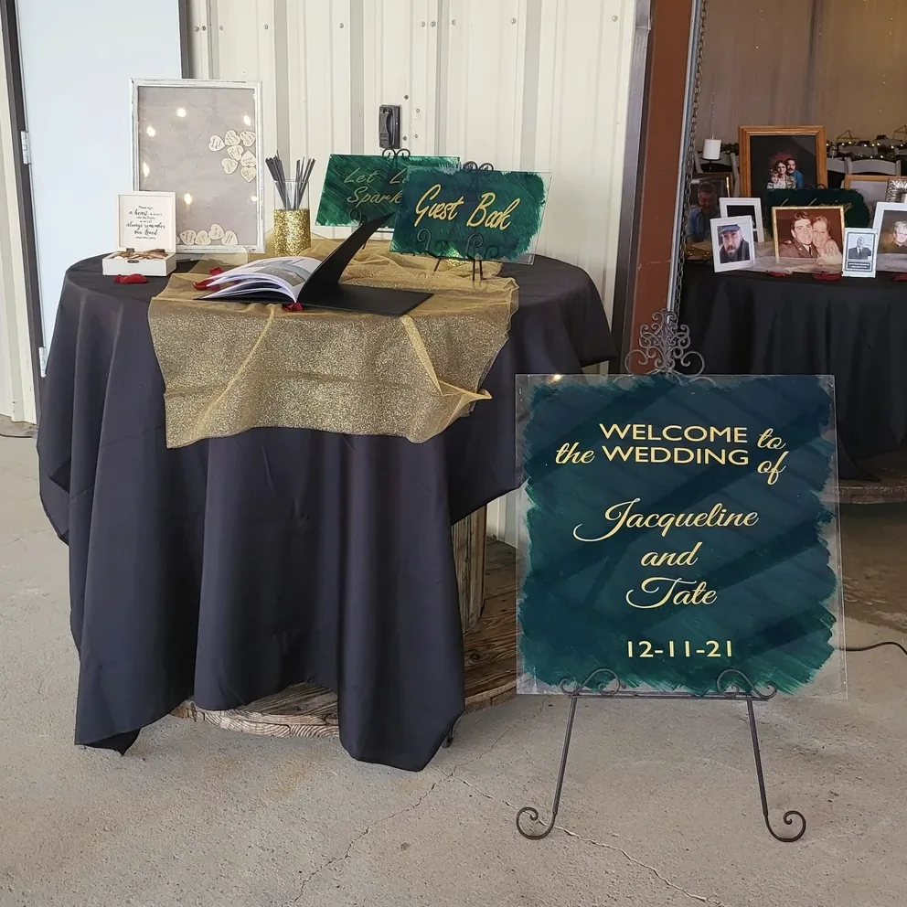 Emerald and gold acrylic wedding welcome sign beside a black and gold guest book table at Reverie at Diamond D