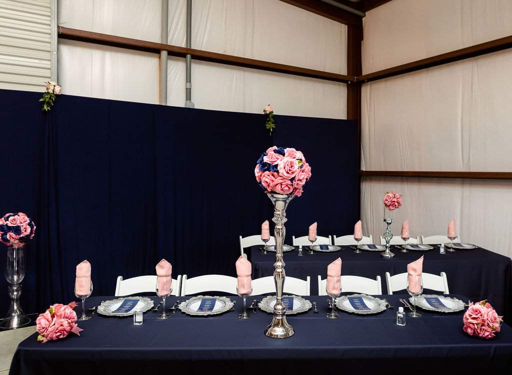 Head table with navy drapery, silver chargers and blush rose arrangements