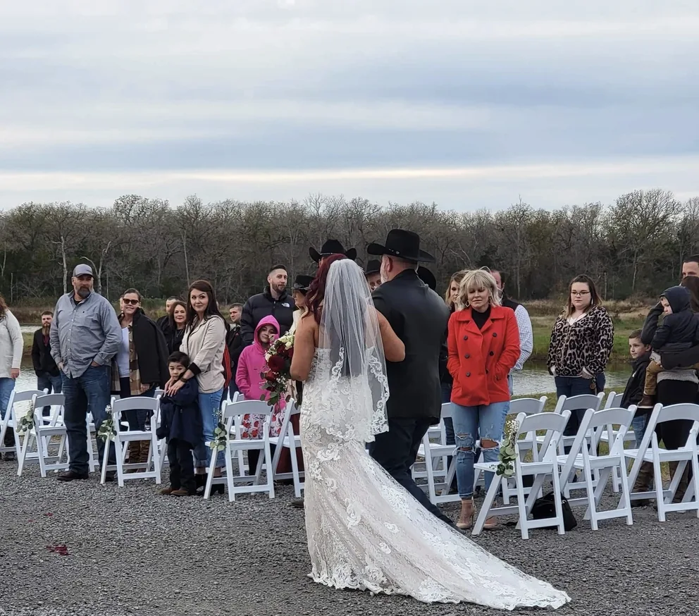 Guests standing along the lakeside aisle as the bride and her father walk toward the ceremony at a Texas country wedding venue