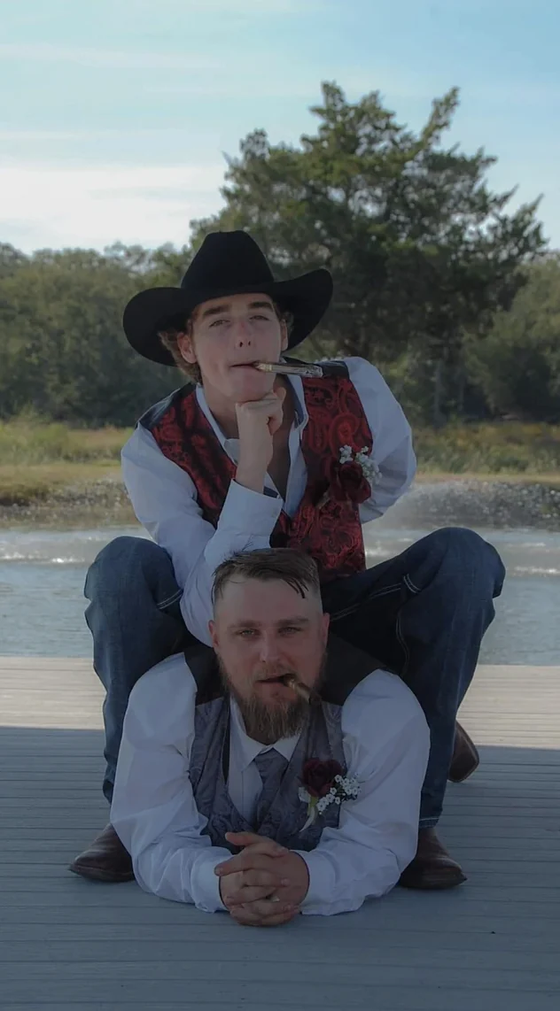 Two groomsmen in cowboy hats posing playfully on the lakeside dock at a Texas wedding venue