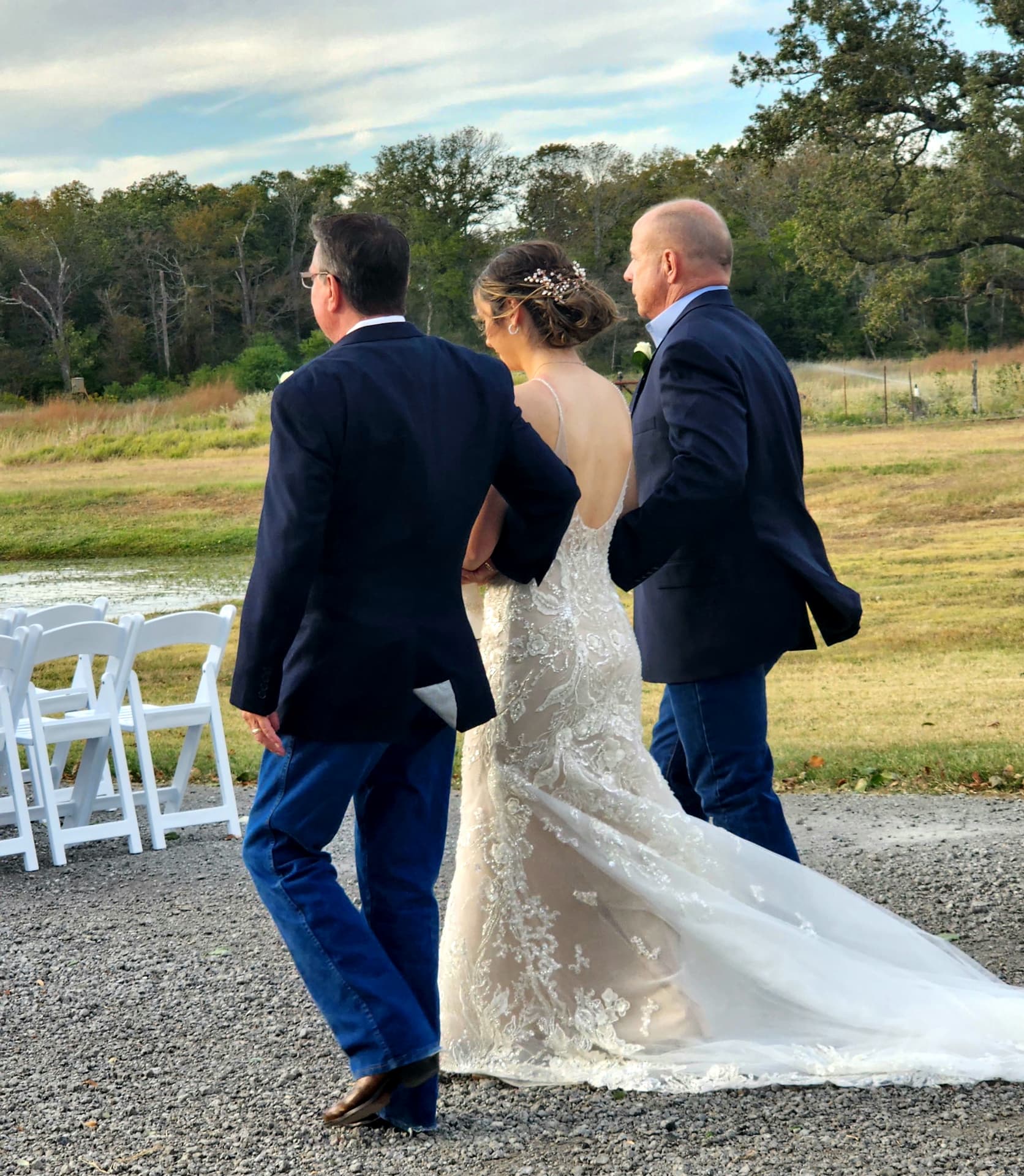 Bride escorted down the lakeside aisle by her fathers in a beaded lace gown
