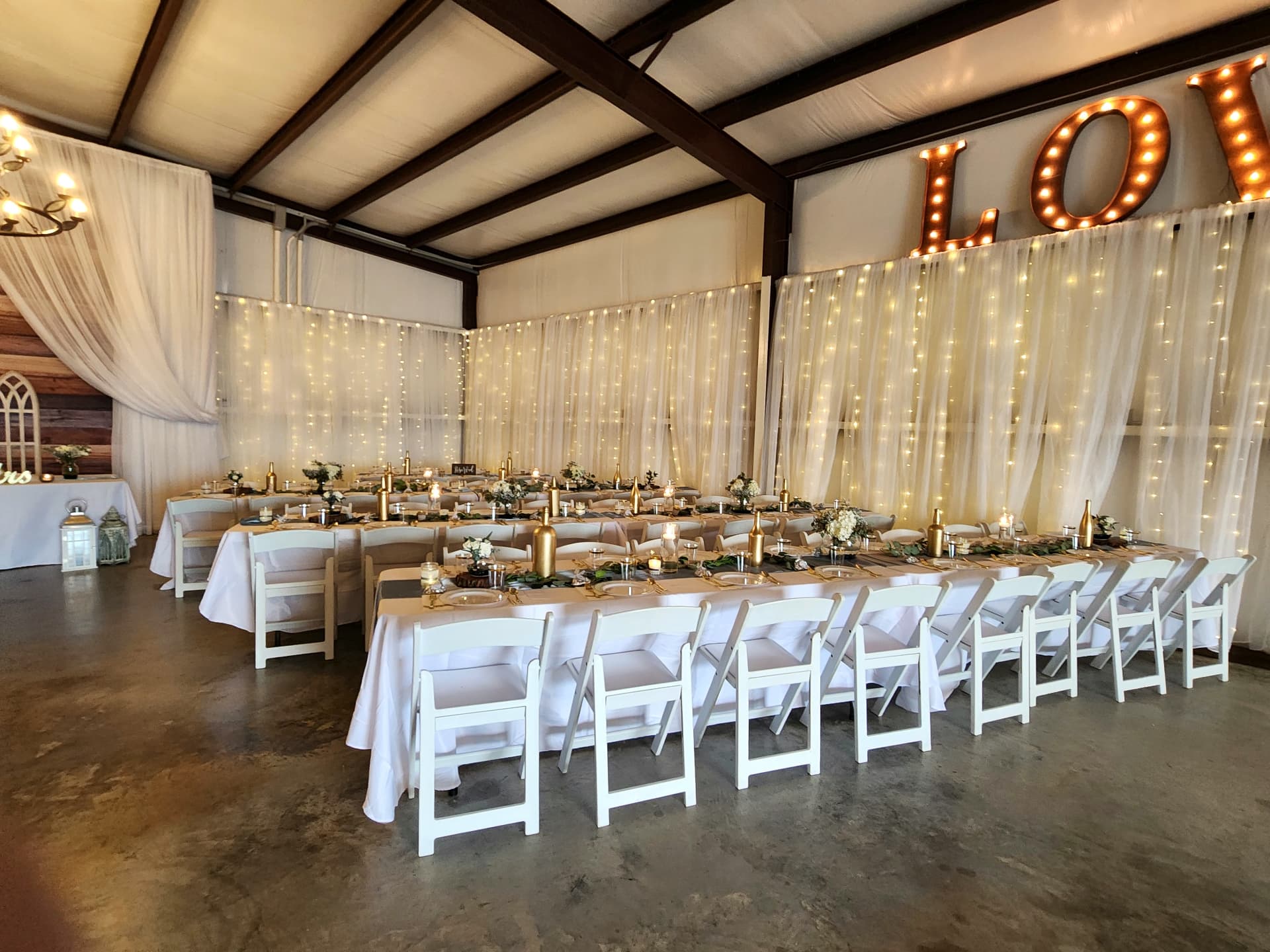 Barn reception with long gold-accented tables, twinkle-light drapery and a LOVE marquee sign