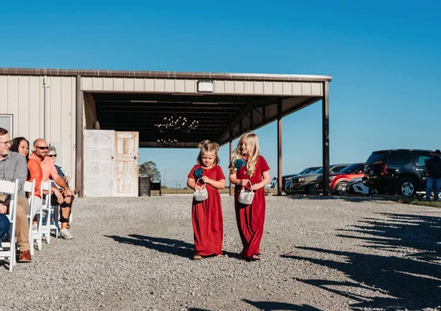 Two flower girls in red dresses walking the gravel aisle with teal petals