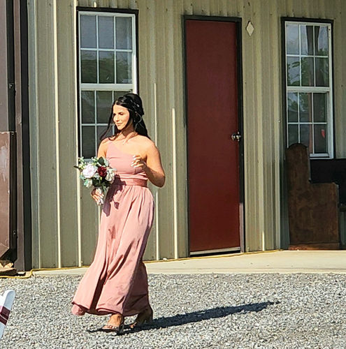 Bridesmaid in a dusty rose gown walking the aisle past the barn at Reverie at Diamond D