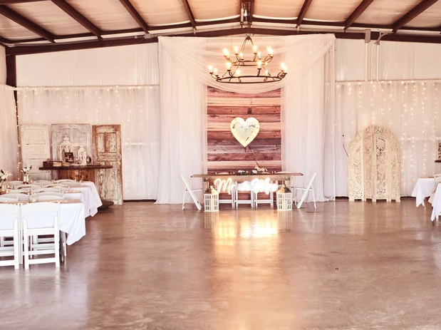 Draped barn reception with wrought-iron chandelier, string lights and a lighted heart backdrop behind the head table