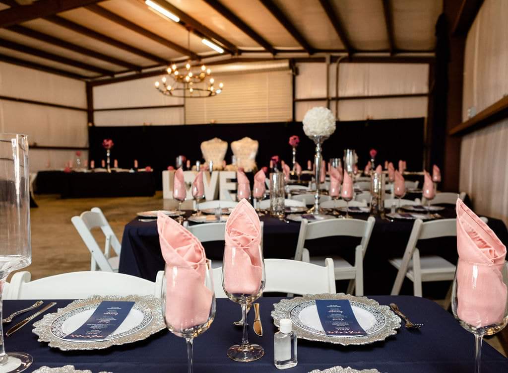 Barn reception with navy linens, blush napkins and silver chargers under chandeliers