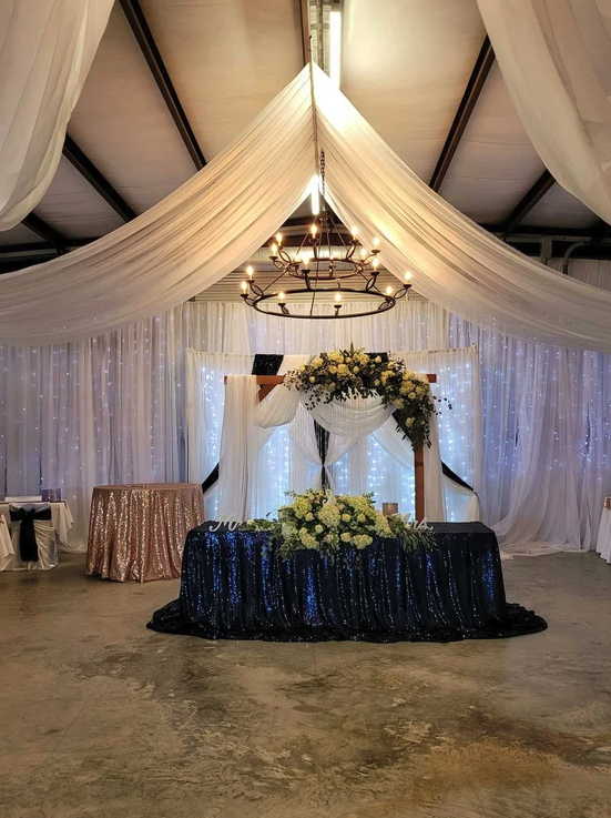 Sweetheart table with navy sequin linen, white florals and chandelier above the draped backdrop