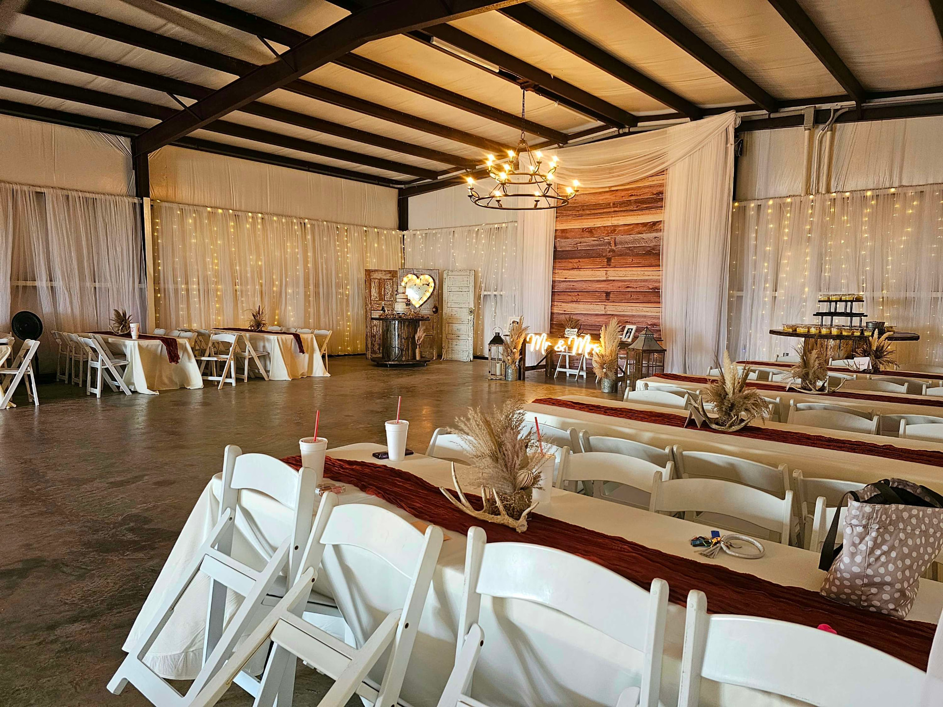 Long wooden reception tables set with candles and greenery inside the draped barn