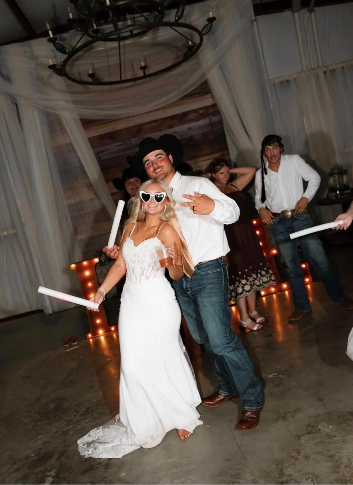 Wedding guests dancing with glow sticks in front of marquee letters during a barn reception at Reverie at Diamond D
