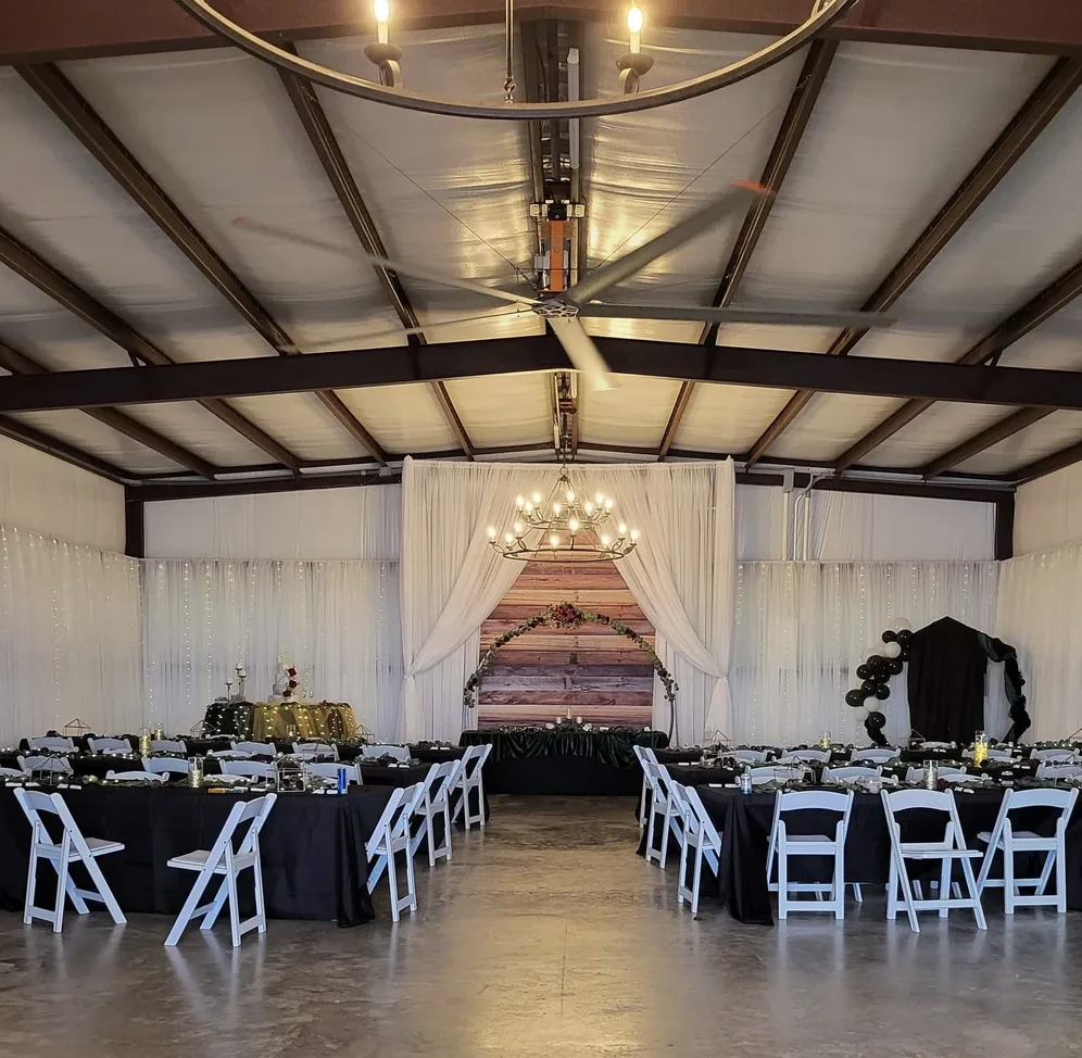 Wedding reception hall with black linens, gold accents, white folding chairs and a chandelier over the head table at Reverie at Diamond D