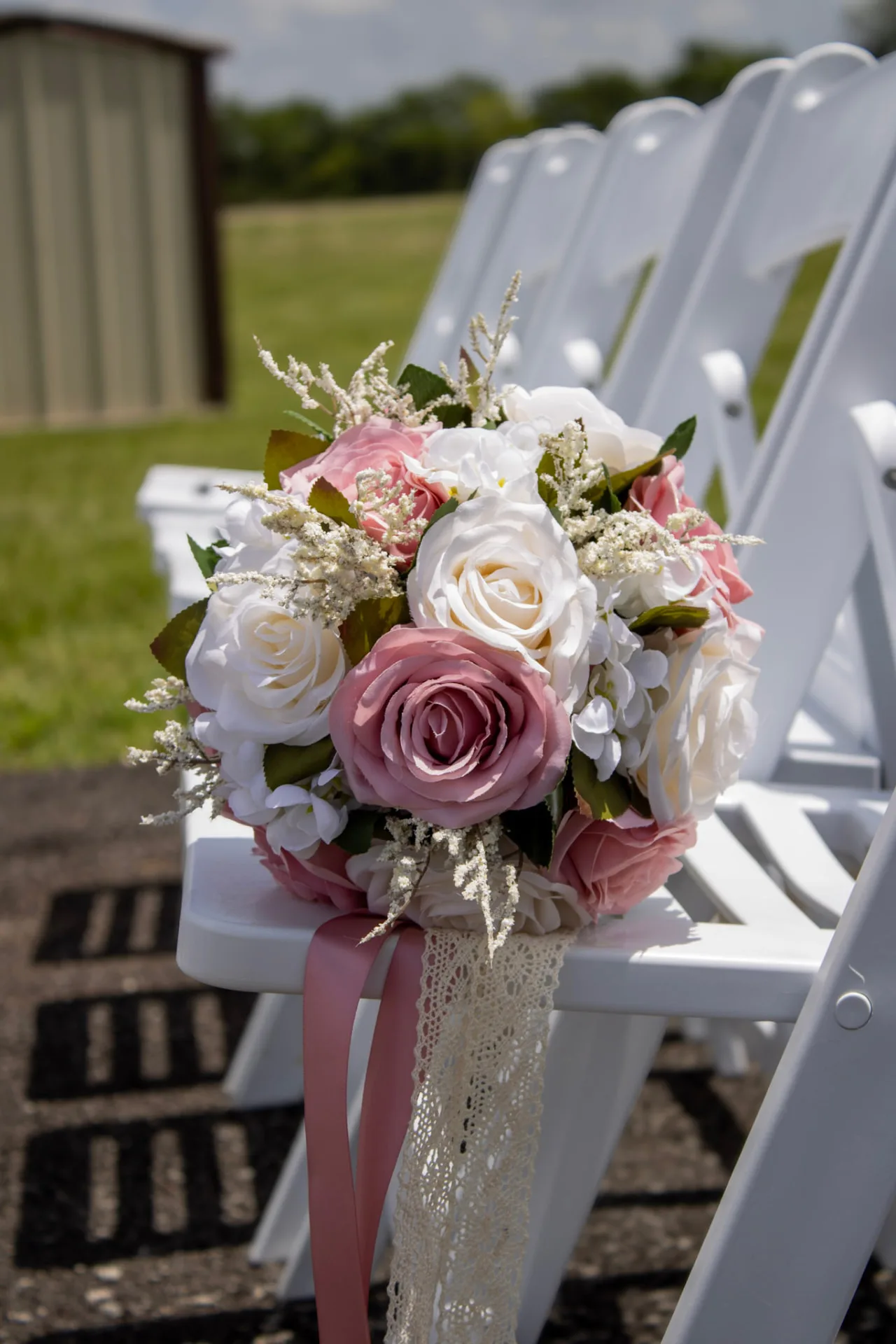 Blush and ivory bridal bouquet resting on a white ceremony chair at Reverie at Diamond D in Normangee, Texas