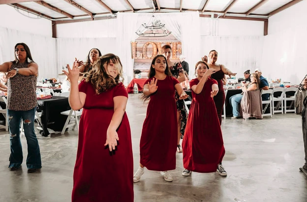 Bridesmaids in red gowns dancing in front of the lighted LOVE marquee in the reception hall