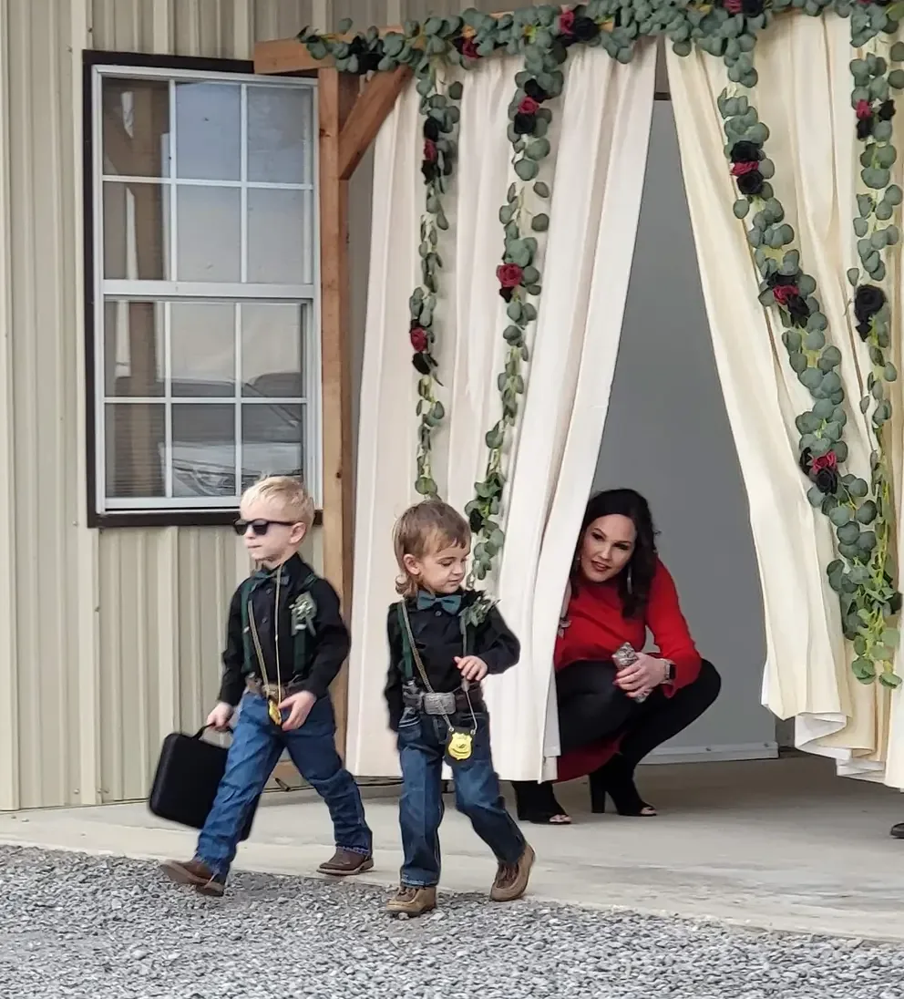 Two young ring bearers in sunglasses walking through the draped ceremony entrance at a Normangee, Texas wedding venue