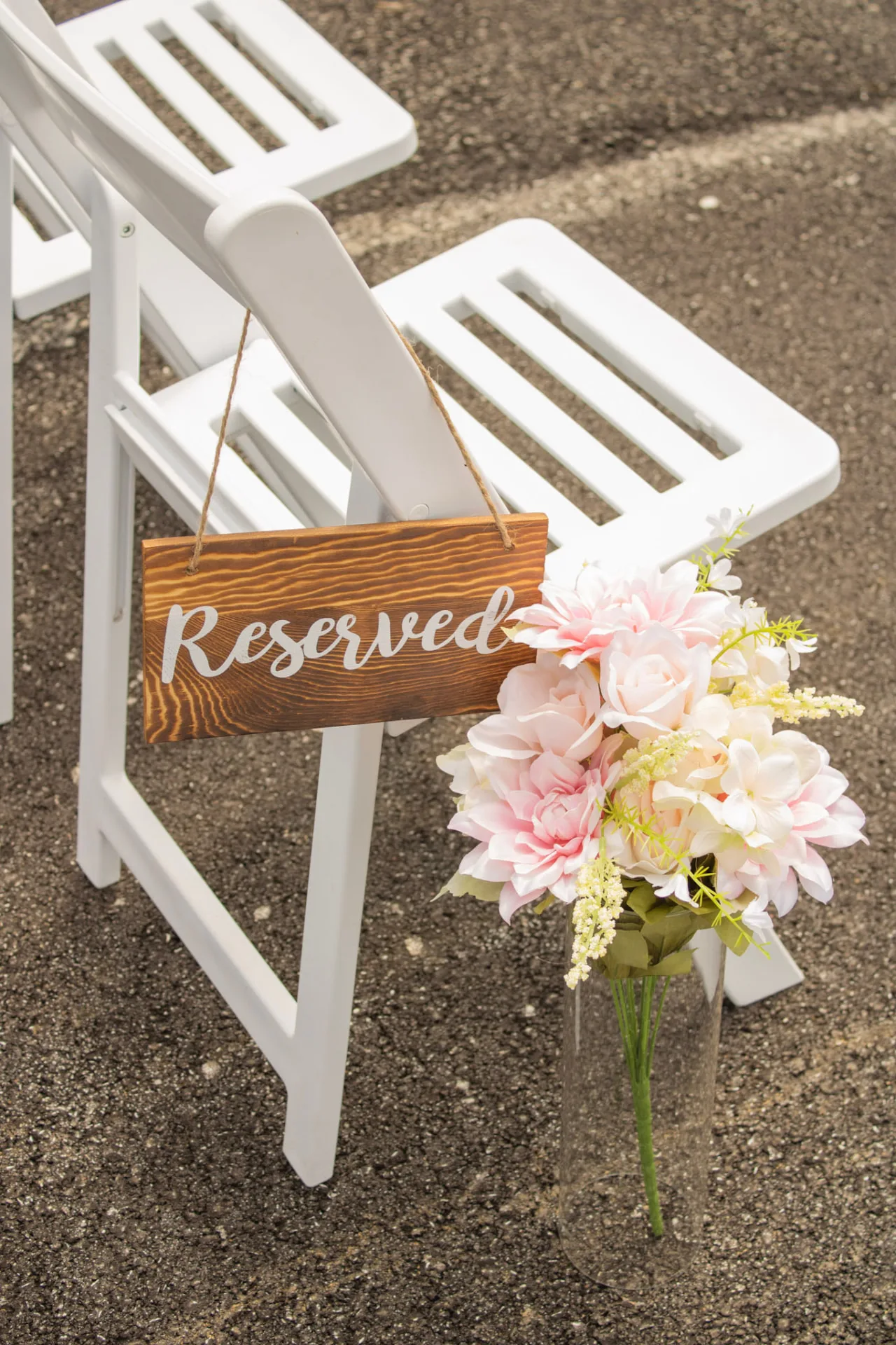 Wooden reserved sign hanging on a white ceremony chair beside a blush floral arrangement
