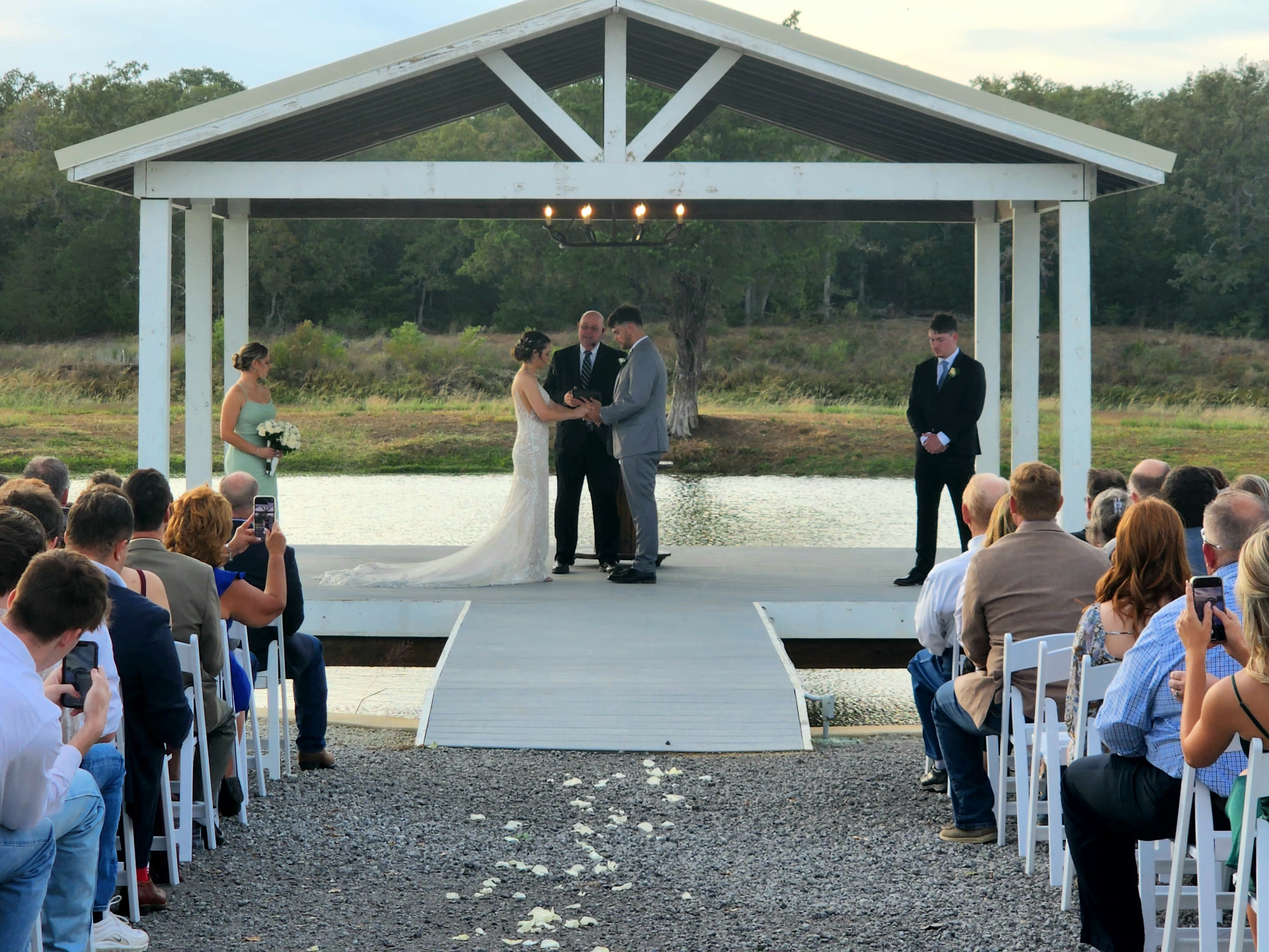 Bride and groom exchanging rings under the lakeside pavilion as guests look on