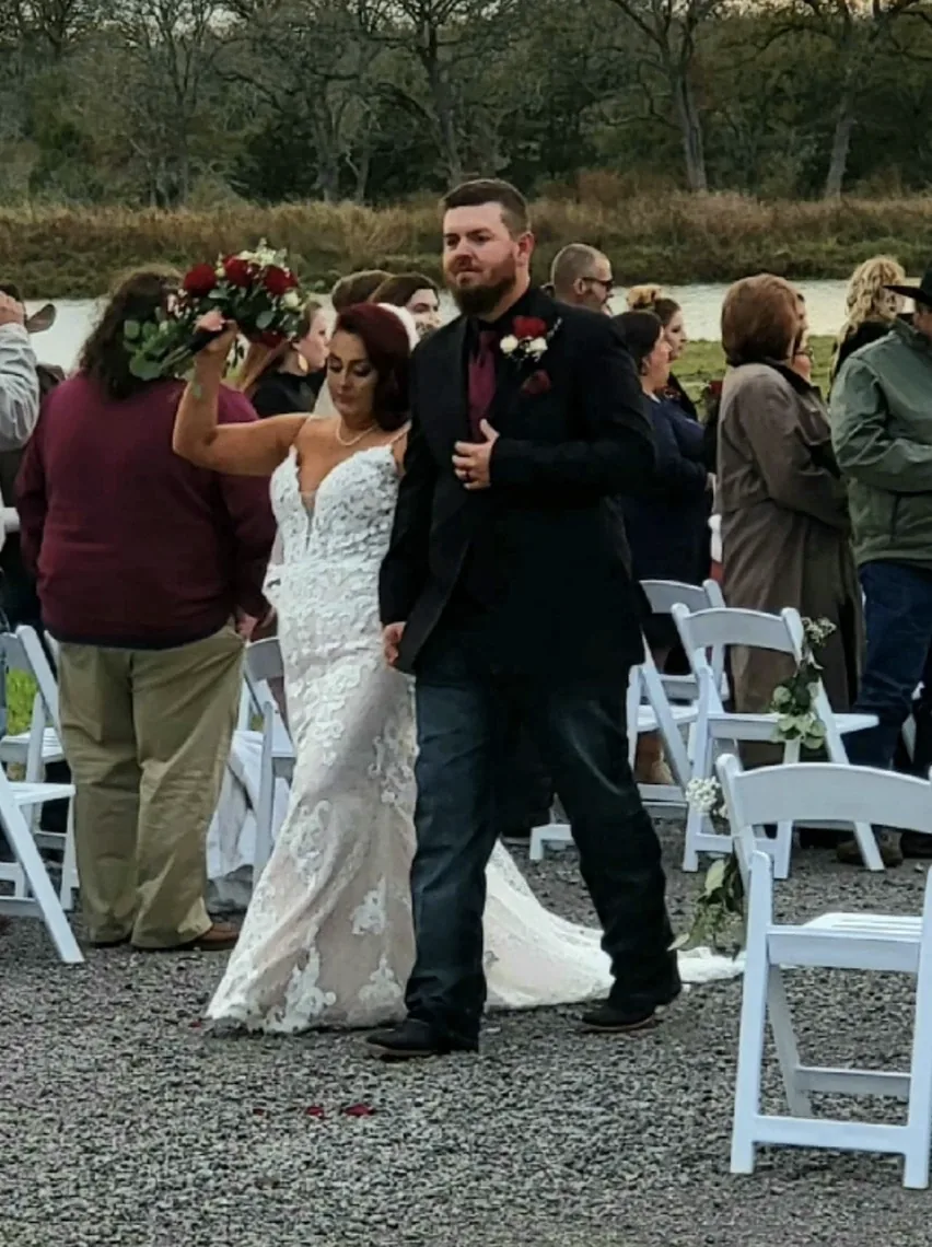 Newlywed bride and groom walking back up the gravel aisle past guests after their lakeside ceremony in Normangee, Texas