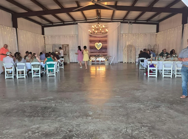 Wide view of the draped barn reception with twinkle-light walls, Mr & Mrs sign and lighted heart backdrop