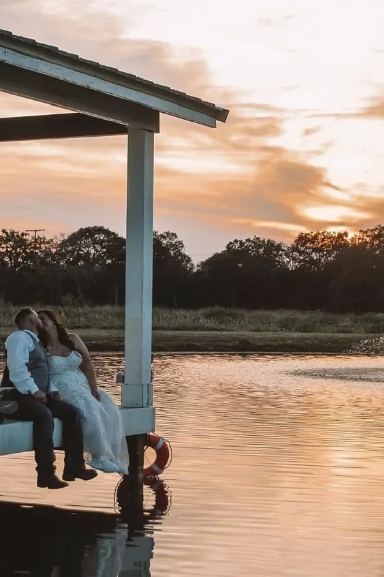 Bride and groom kissing on the dock at sunset with the lake glowing behind them at a Texas wedding venue