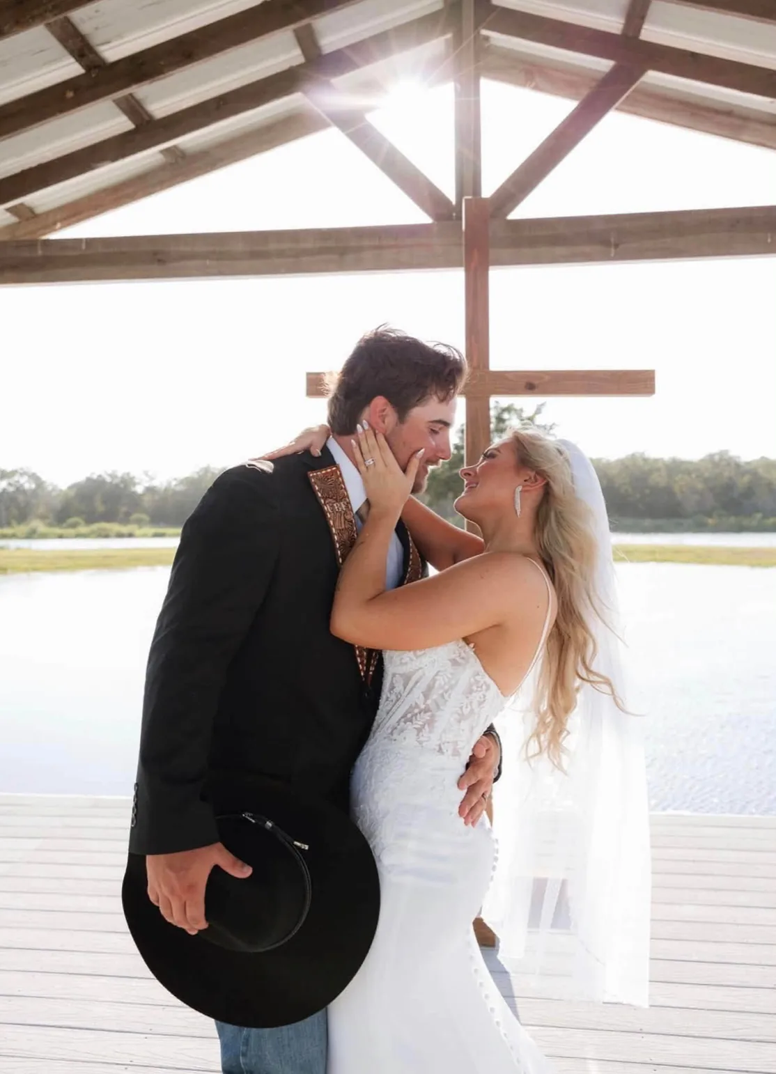 Cannon and Caroline embracing beneath the wooden cross on the lakeside pavilion at Reverie at Diamond D in Normangee, Texas