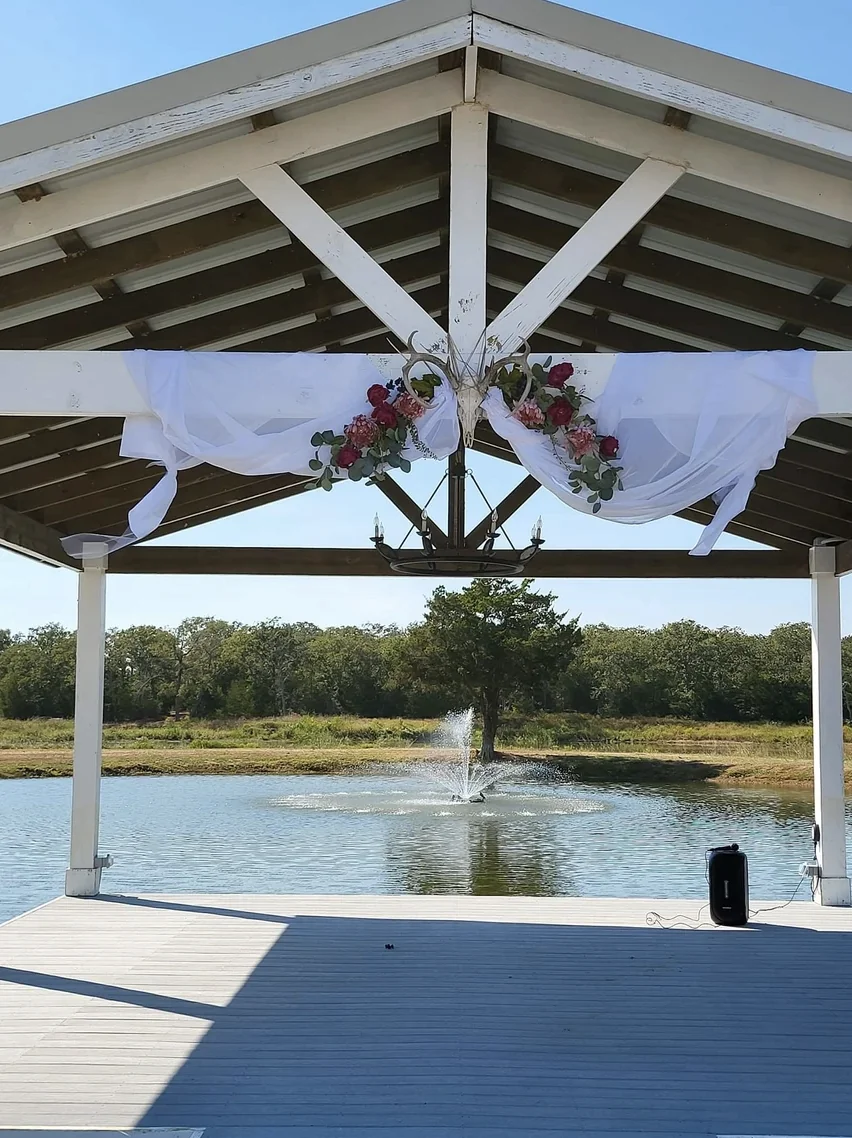 Draped lakeside pavilion decorated with white chiffon, roses and a chandelier before the ceremony at Reverie at Diamond D in Normangee, Texas