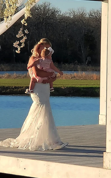 Bride holding her flower girl on the pavilion dock overlooking the lake