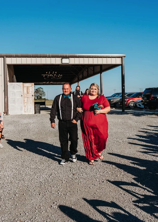 Mother of the bride in a red gown escorted across the gravel aisle before the ceremony