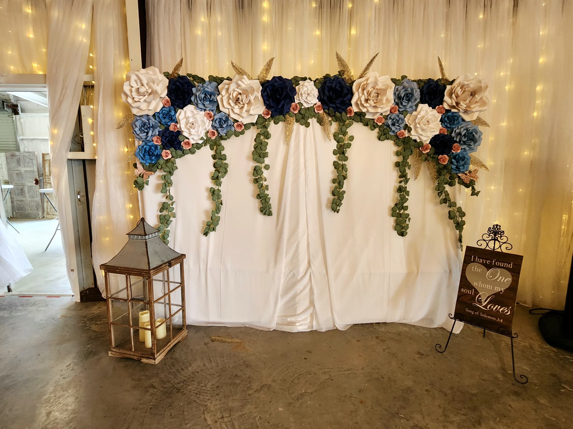 Handmade paper flower backdrop in navy, blush and ivory against twinkle-light drapery