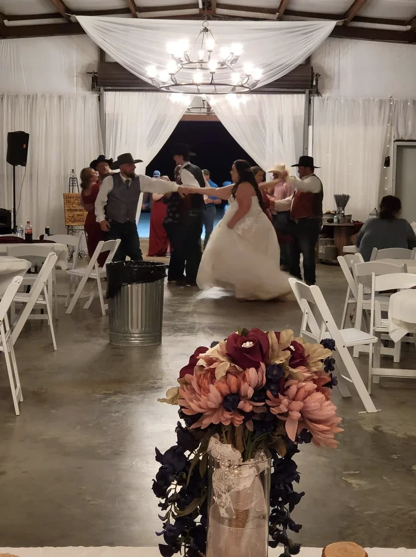 Cole and Emily sharing their first dance under the chandeliers in the draped reception barn at Reverie at Diamond D