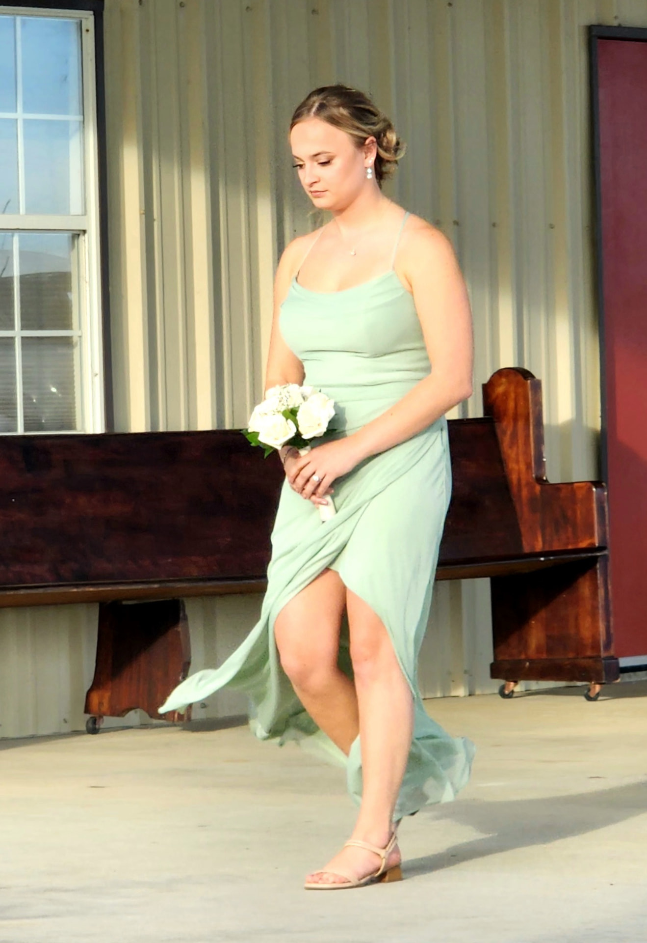 Bridesmaid in a sage green gown walking the processional past the barn at Reverie at Diamond D