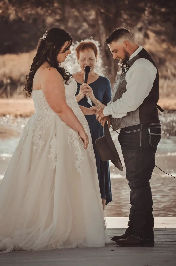 Bride and groom exchanging rings on the lakeside dock while the officiant reads the vows