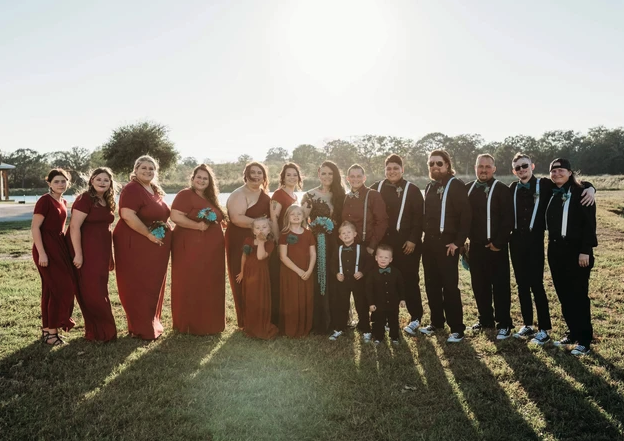 Full wedding party in burgundy and teal posing on the lawn at golden hour