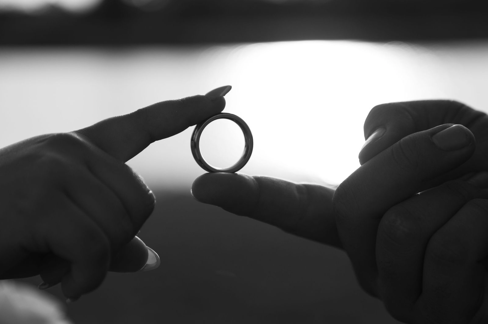 Jaelyn & Keelan's wedding at Reverie at Diamond D — black-and-white close-up of hands holding a wedding ring against the sky