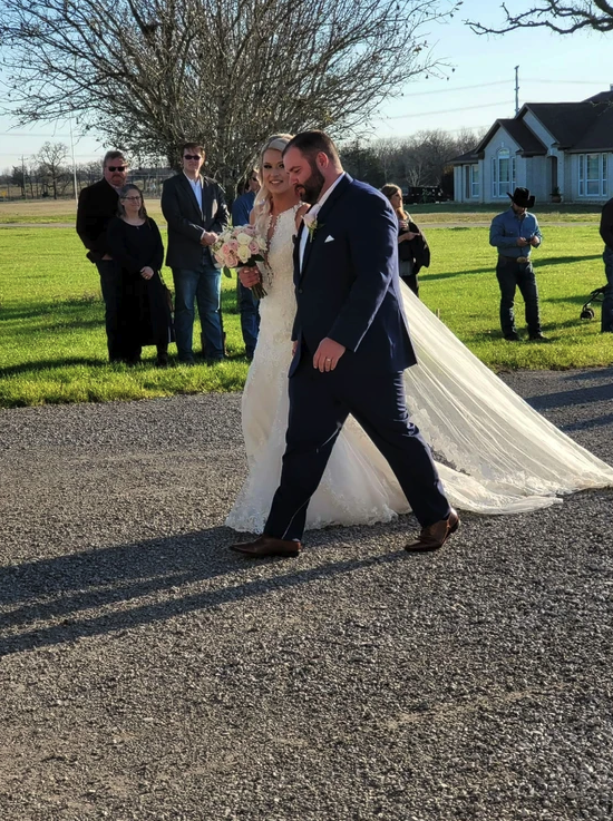 Newlyweds walking toward the farmhouse with the bride's cathedral train trailing behind