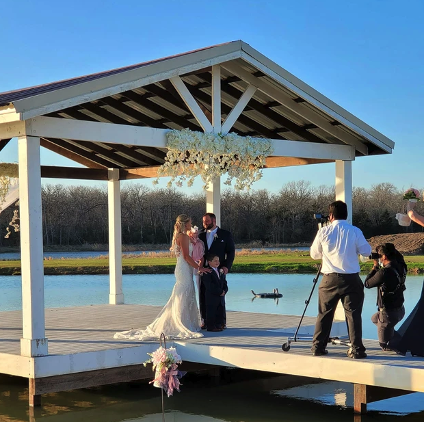 Bride and groom with their children on the lakeside dock under the floral chandelier