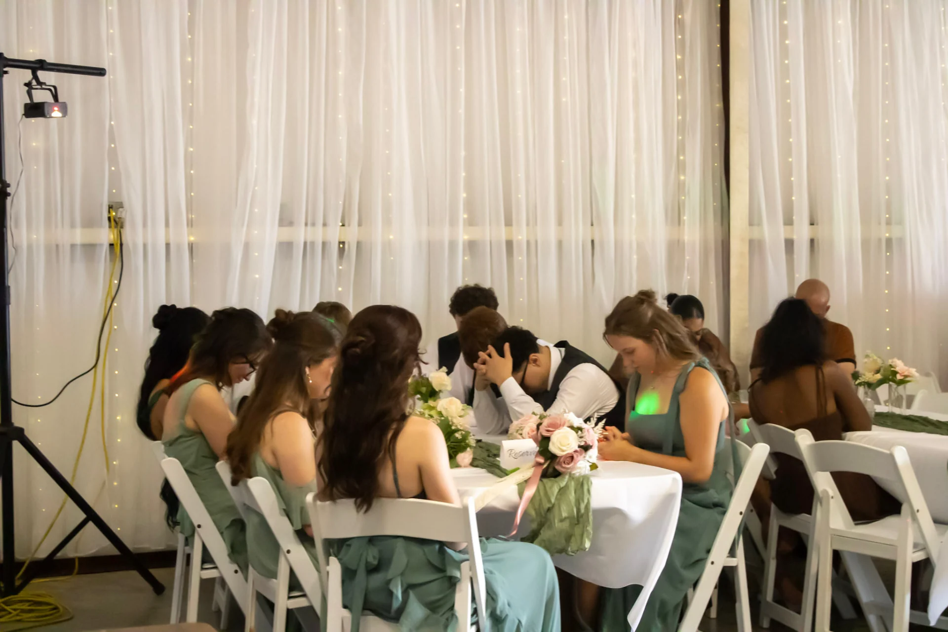 Wedding party seated at the head table in front of string light draping during the reception