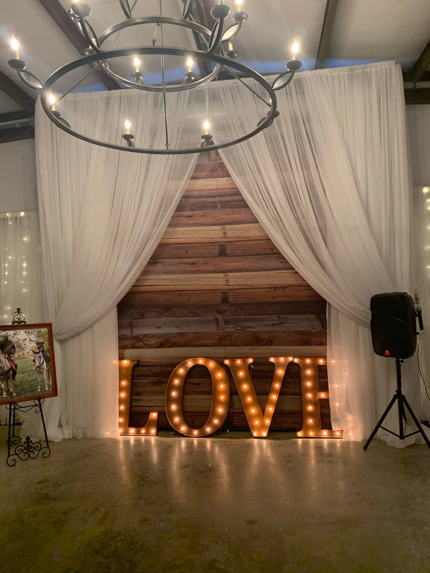 Lighted marquee LOVE letters in front of a reclaimed barn wood wall framed by white drapery at the Love Like Bailin Therapy Farm event
