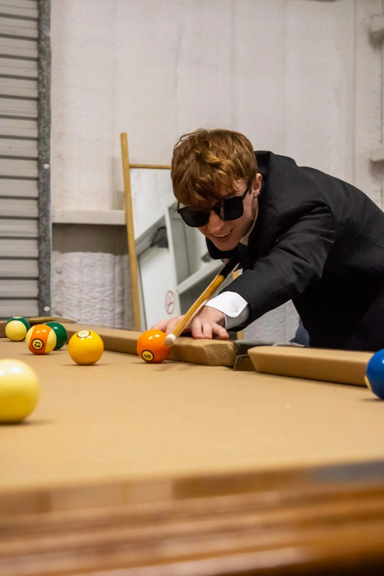 Groomsman in sunglasses taking a shot at the pool table during the wedding day