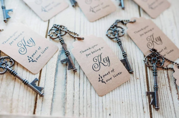 Vintage key bottle opener wedding favors with kraft thank-you tags on whitewashed wood