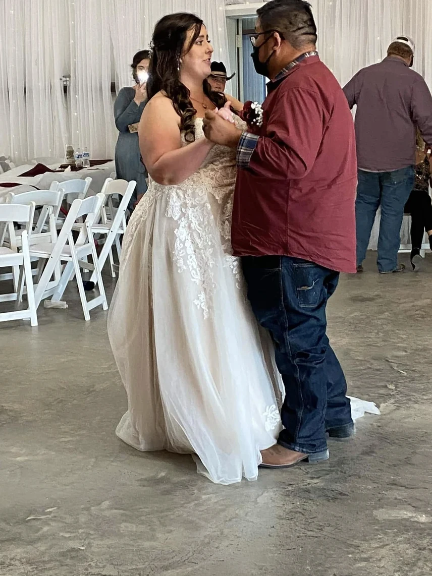 Emily dancing with her father among white chairs and burgundy table settings inside the reception hall