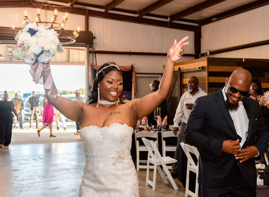 Bride raising her bouquet in celebration as she enters the barn reception