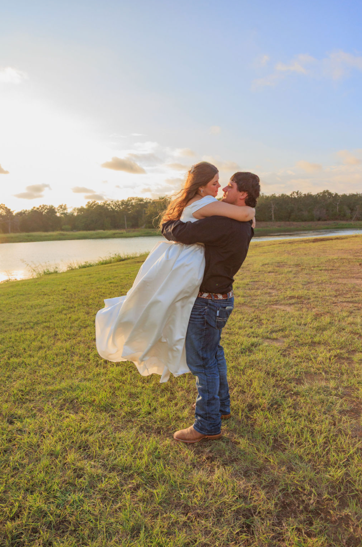 Jaelyn & Keelan's wedding at Reverie at Diamond D — the groom lifting the bride in an embrace by the lake at sunset