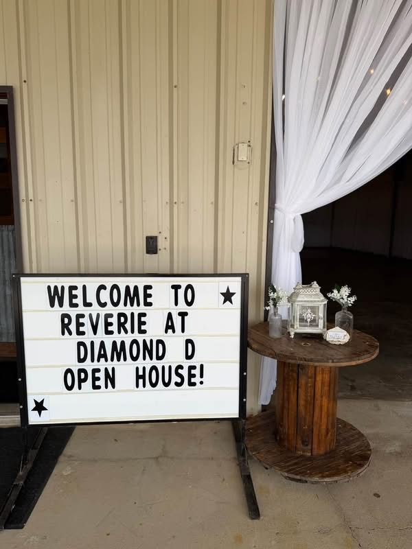 October 2026 Open House at Reverie at Diamond D wedding venue in Normangee, Texas — the letter-board welcome sign beside a wooden spool table with a lantern