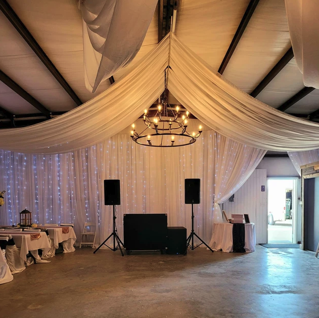 Open barn dance floor with DJ setup, chandelier and curtain-light backdrop at Reverie at Diamond D
