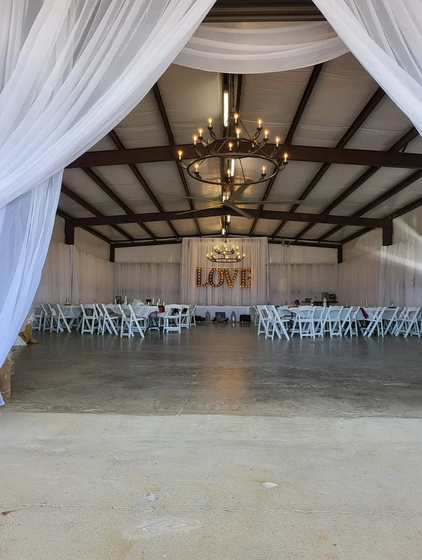 View through white draped entrance curtains into the reception hall with a lit LOVE sign and head table at Reverie at Diamond D