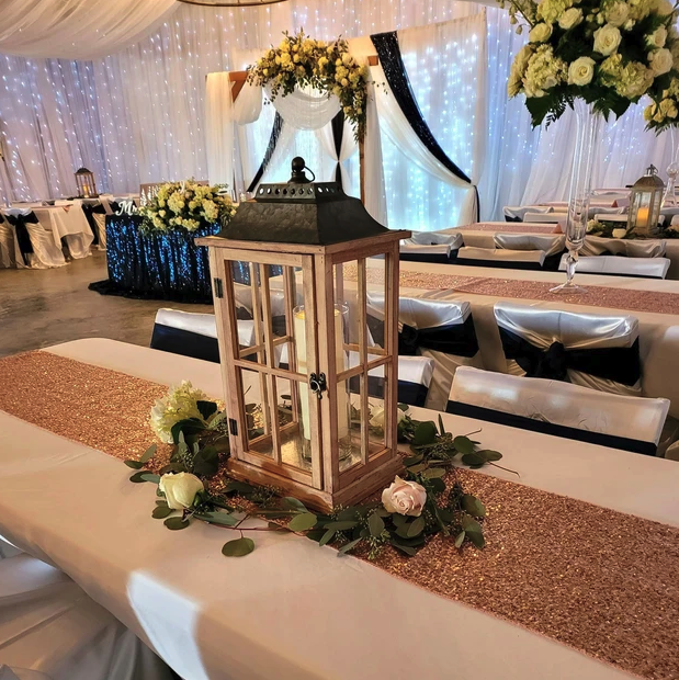 Wooden lantern centerpiece with roses and eucalyptus on a rose gold sequin table runner