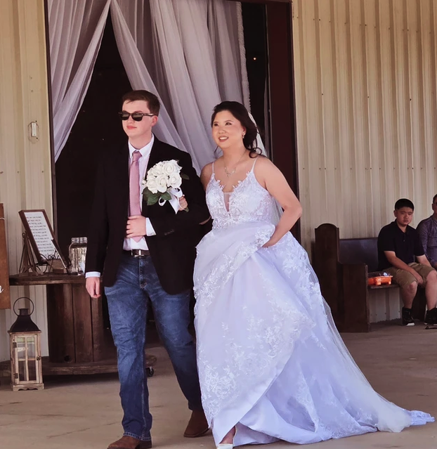 Bride escorted through the draped barn entrance carrying a white rose bouquet