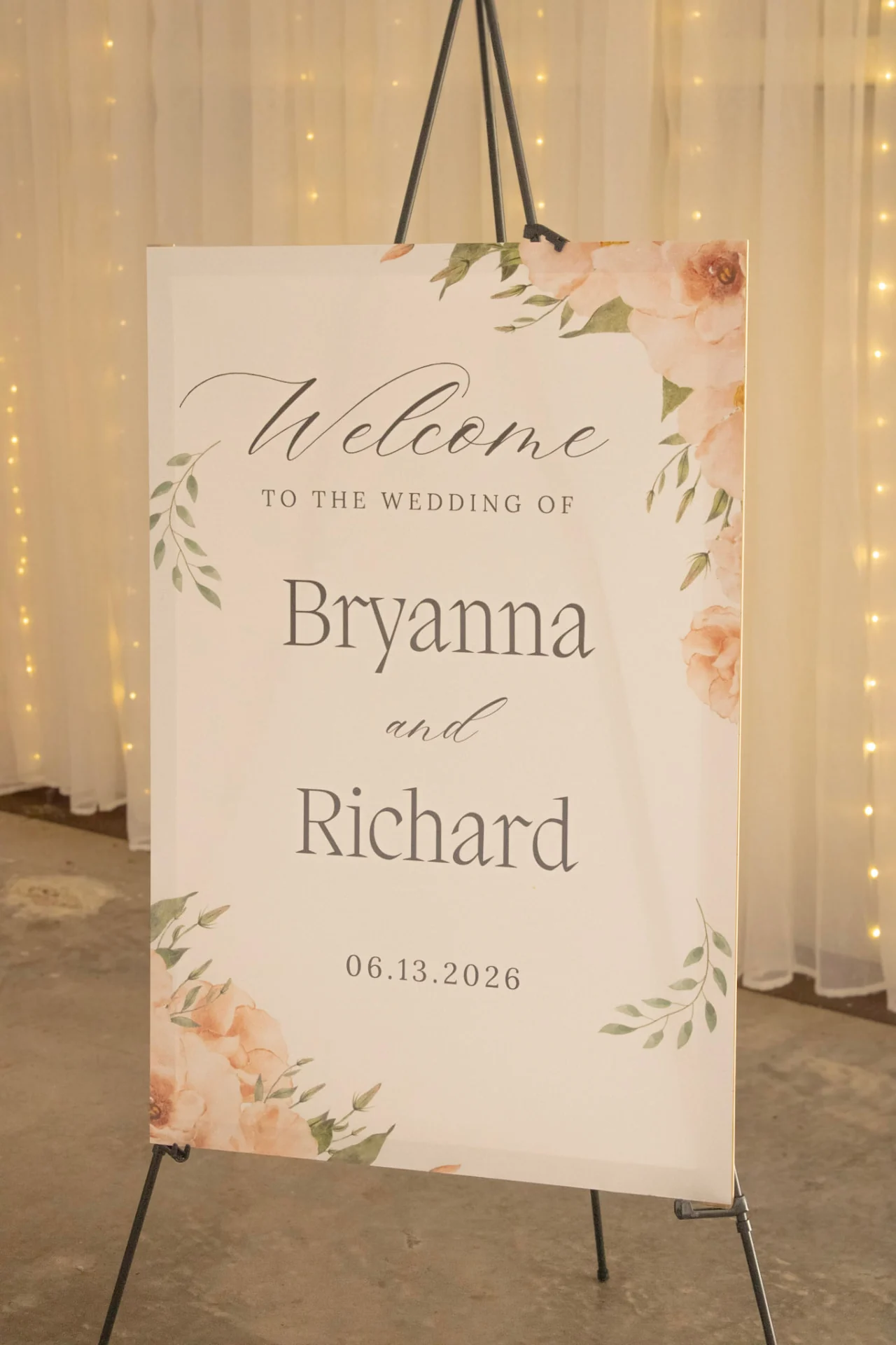 Floral welcome sign for Bryanna and Richard's June 13, 2026 wedding on an easel in front of twinkle-lit draping at Reverie at Diamond D