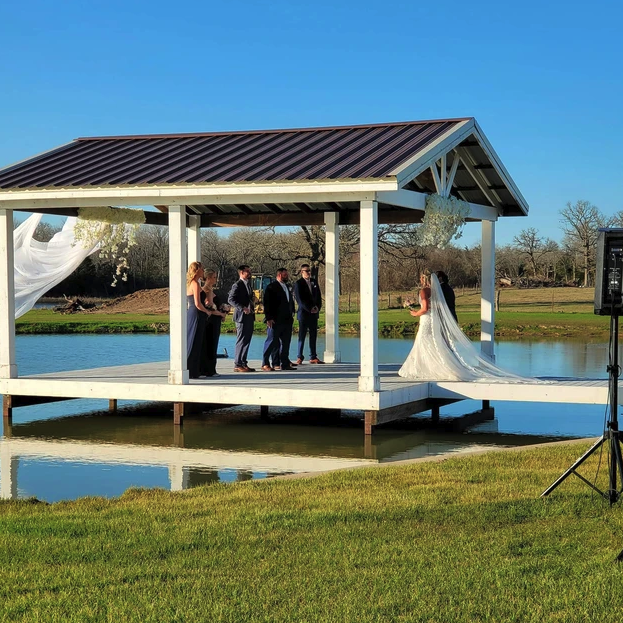 Wide view of the white lakeside ceremony pavilion mirrored in the water during the wedding